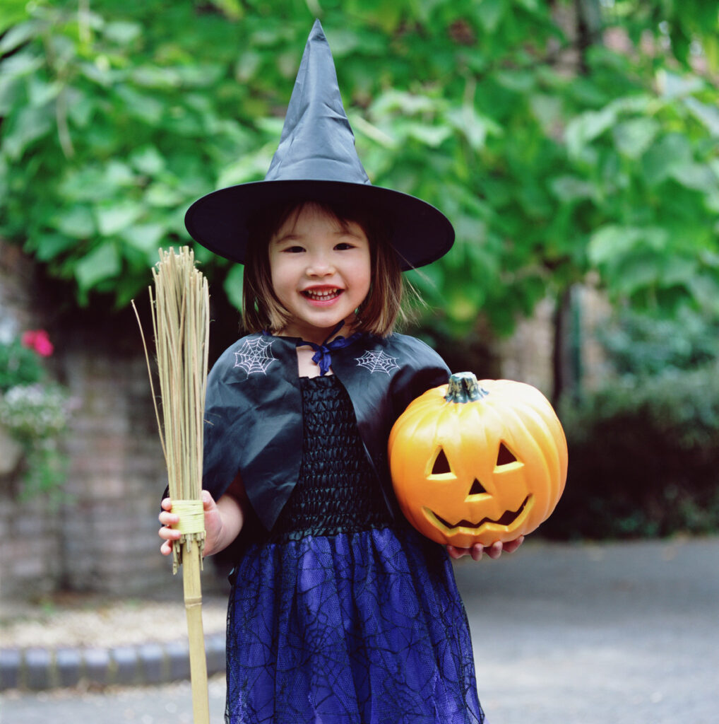 Girl in witch costume with broom and jack o'-lantern