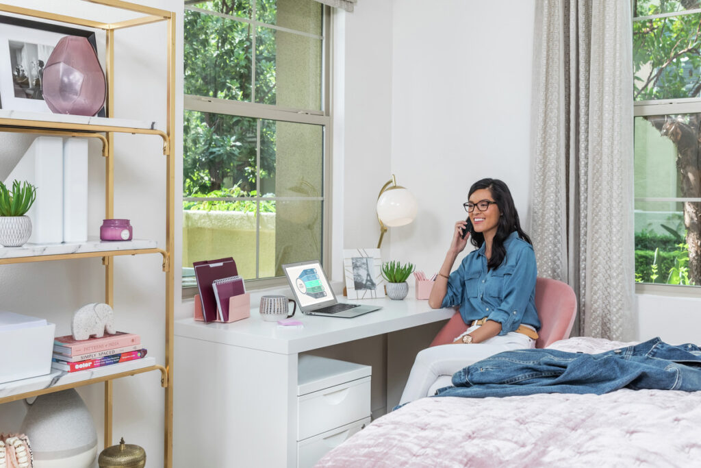 Woman taking a call and working off of a laptop in her bedroom