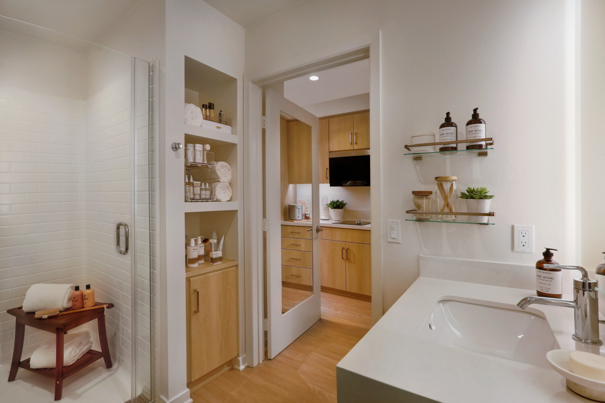 View of bathroom amenities in Meridian Apartment unit with door open to partial view of the kitchen amenities